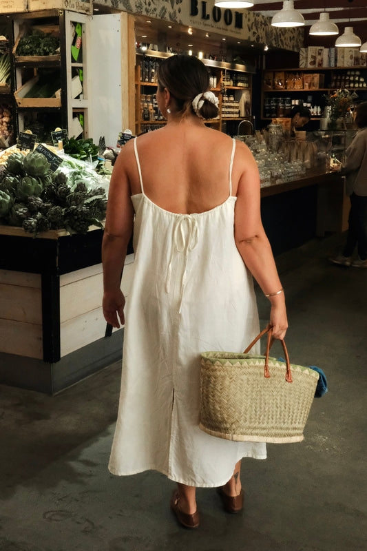 Woman in a white dress holding a basket in a market setting